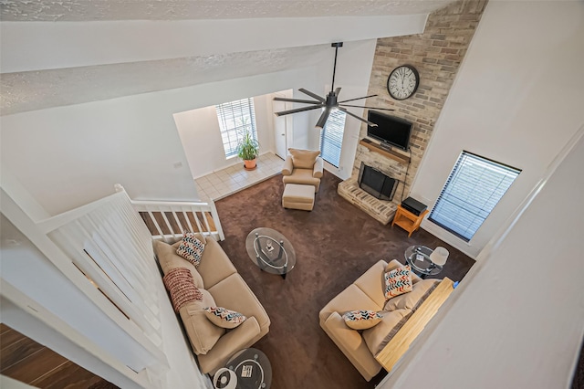 living area with a ceiling fan, a brick fireplace, vaulted ceiling with beams, and a textured ceiling