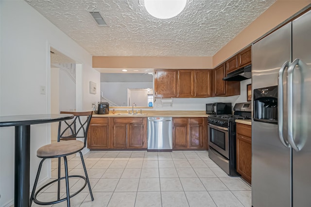 kitchen with visible vents, brown cabinets, stainless steel appliances, under cabinet range hood, and light tile patterned flooring