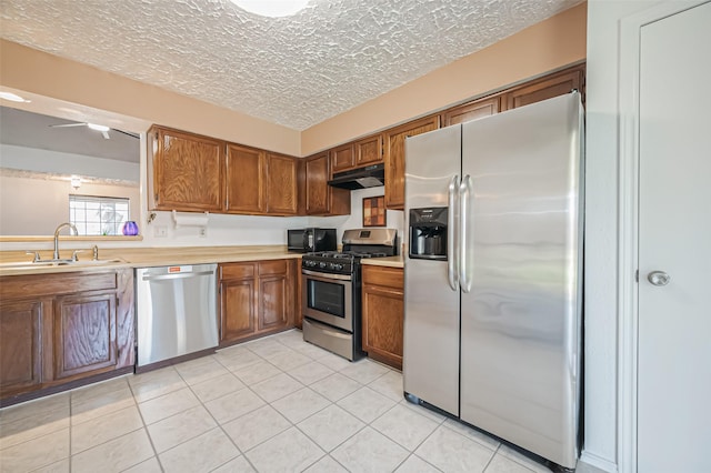 kitchen featuring under cabinet range hood, stainless steel appliances, a sink, light countertops, and brown cabinets