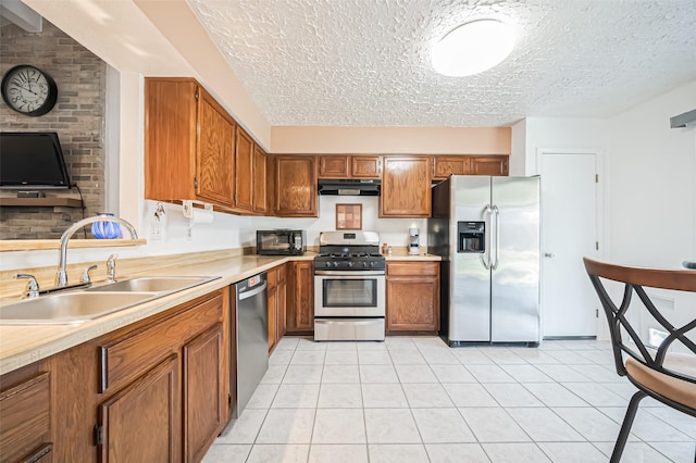 kitchen with a sink, appliances with stainless steel finishes, brown cabinets, and under cabinet range hood