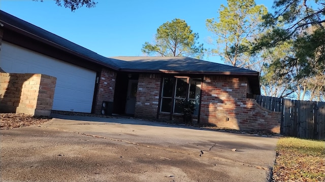 ranch-style house featuring an attached garage, driveway, fence, and brick siding