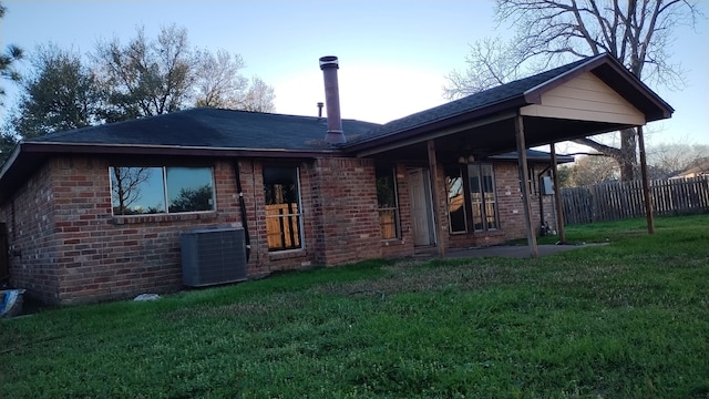 rear view of property with brick siding, a lawn, central AC unit, and fence