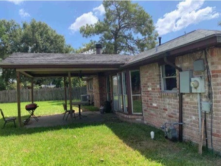 rear view of property featuring a yard, brick siding, a patio, and fence