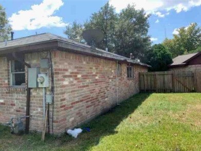 view of property exterior featuring fence, a lawn, and brick siding