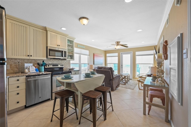 kitchen featuring light tile patterned floors, tasteful backsplash, appliances with stainless steel finishes, crown molding, and cream cabinetry