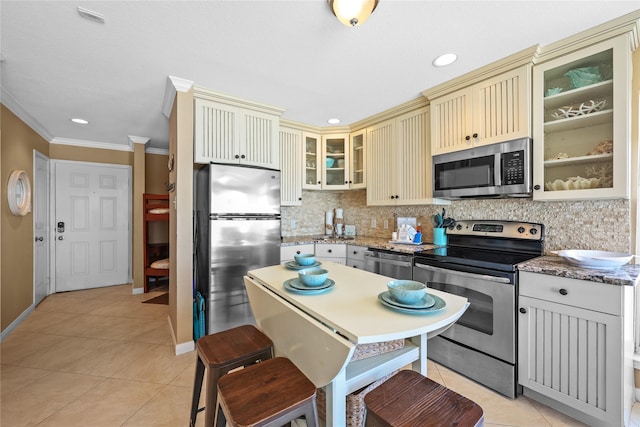 kitchen with light tile patterned floors, appliances with stainless steel finishes, cream cabinets, and backsplash