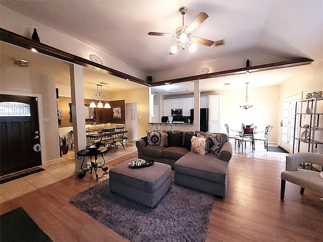 living room featuring ceiling fan with notable chandelier, lofted ceiling, visible vents, and wood finished floors