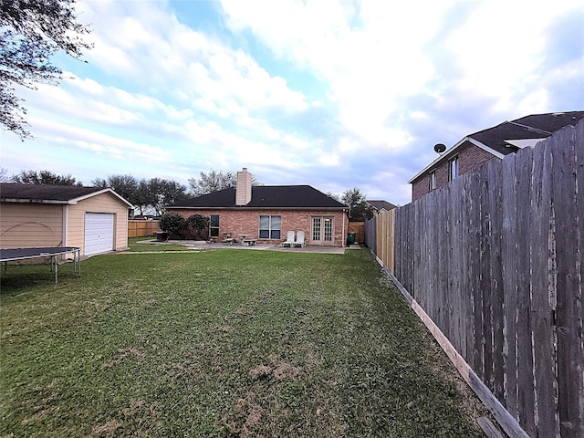 view of yard with a trampoline, a patio area, a garage, a fenced backyard, and an outdoor structure