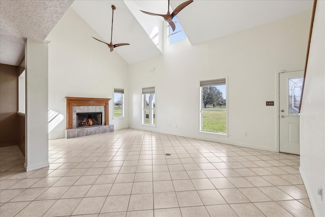 unfurnished living room with a fireplace, a ceiling fan, light tile patterned flooring, high vaulted ceiling, and baseboards