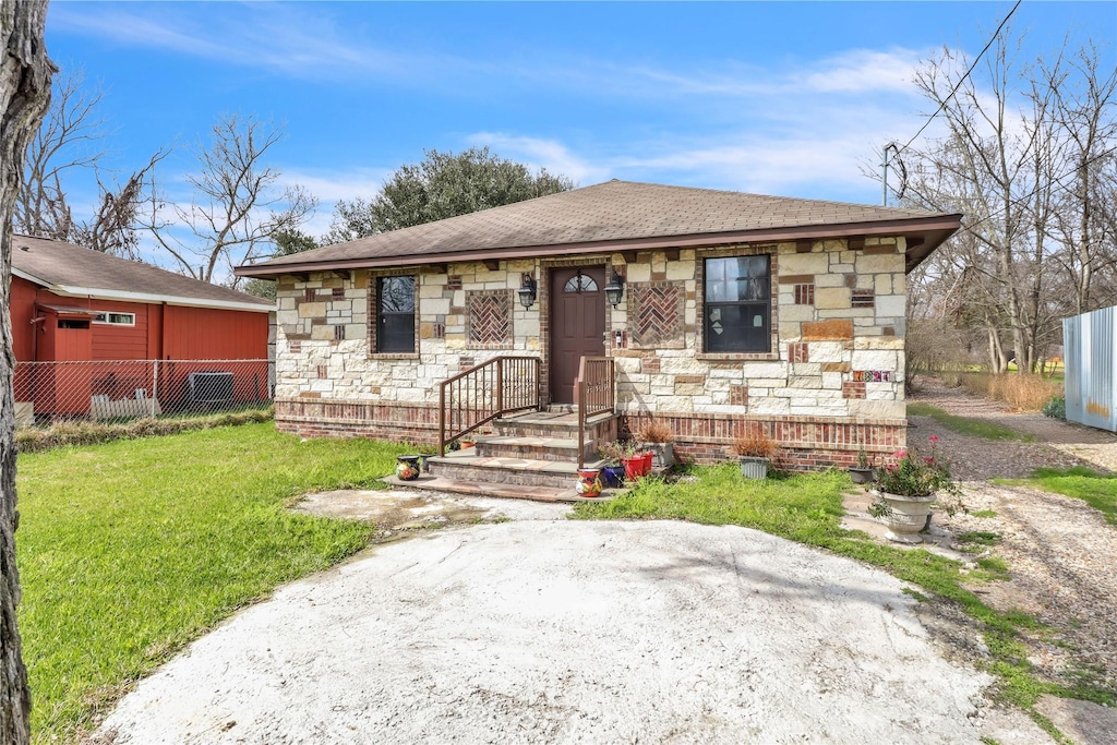 bungalow featuring stone siding, a front yard, and fence