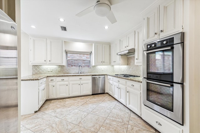 kitchen with light stone counters, stainless steel appliances, tasteful backsplash, white cabinetry, and under cabinet range hood