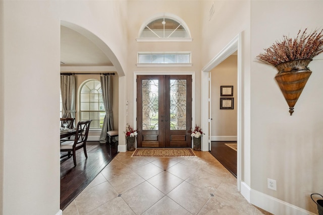 entrance foyer featuring light tile patterned floors, french doors, a towering ceiling, and baseboards