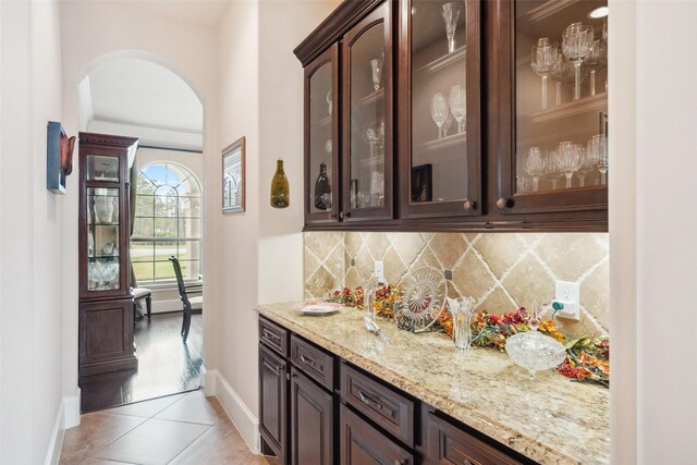 bar featuring arched walkways, a dry bar, light tile patterned floors, decorative backsplash, and baseboards