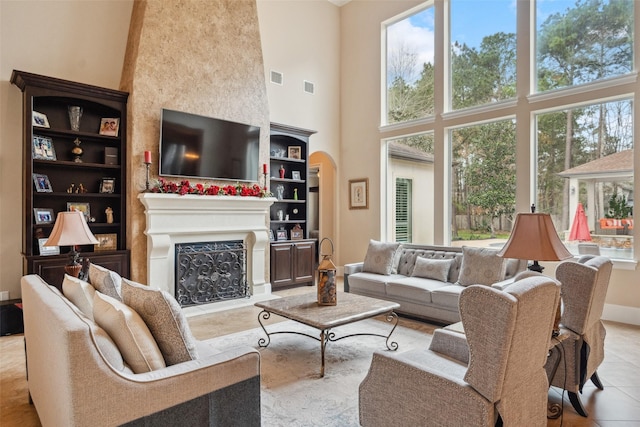 living area with arched walkways, visible vents, a fireplace, and a towering ceiling