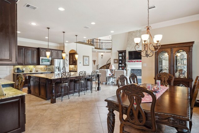 dining space featuring ornamental molding, a fireplace, visible vents, and a notable chandelier