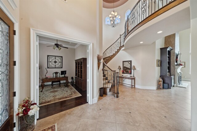 entrance foyer featuring a towering ceiling, stairs, baseboards, and ceiling fan with notable chandelier