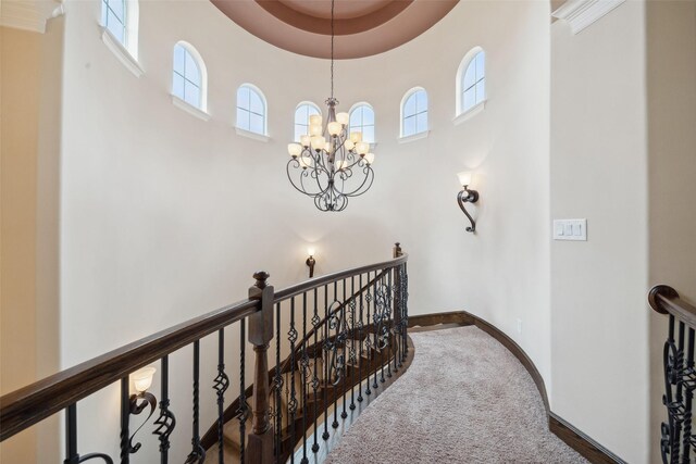 hallway with a notable chandelier, carpet floors, a towering ceiling, baseboards, and an upstairs landing