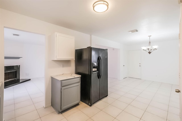 kitchen with visible vents, a fireplace with raised hearth, light tile patterned flooring, a chandelier, and black fridge