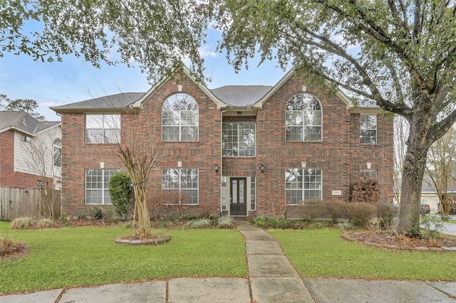 view of front facade with brick siding, fence, and a front lawn