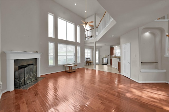 unfurnished living room with ceiling fan, baseboards, a tiled fireplace, and wood finished floors