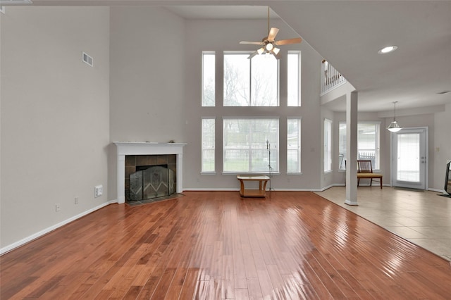 unfurnished living room with baseboards, visible vents, a tile fireplace, wood finished floors, and a high ceiling