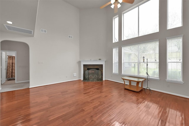 unfurnished living room featuring arched walkways, wood finished floors, visible vents, and a tile fireplace