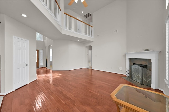 unfurnished living room with visible vents, arched walkways, a ceiling fan, a tiled fireplace, and hardwood / wood-style flooring