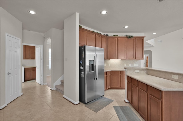 kitchen with tasteful backsplash, arched walkways, brown cabinetry, stainless steel fridge with ice dispenser, and light countertops