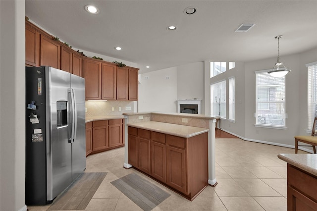 kitchen with a center island, visible vents, decorative backsplash, brown cabinets, and stainless steel fridge