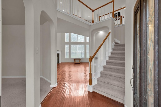 entrance foyer with arched walkways, hardwood / wood-style flooring, a towering ceiling, baseboards, and stairway