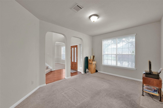 interior space featuring arched walkways, visible vents, baseboards, stairs, and carpet