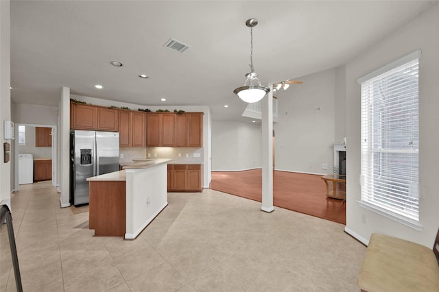 kitchen with stainless steel refrigerator with ice dispenser, light countertops, visible vents, open floor plan, and washer / dryer