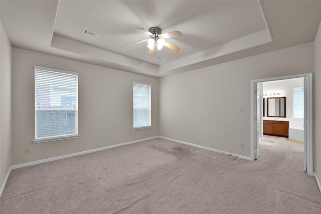 unfurnished room featuring baseboards, visible vents, a raised ceiling, light colored carpet, and ceiling fan