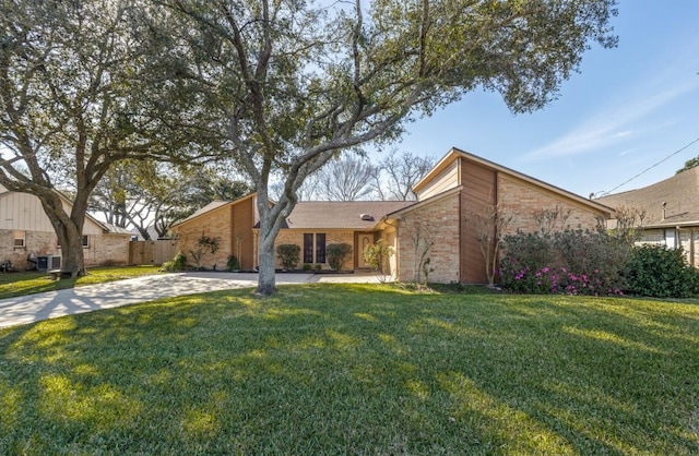 mid-century modern home featuring central air condition unit, brick siding, concrete driveway, and a front yard