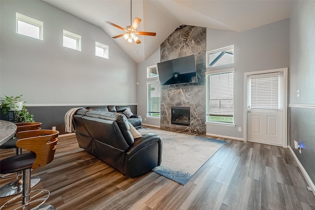 living area with a fireplace, ceiling fan, wood finished floors, high vaulted ceiling, and baseboards