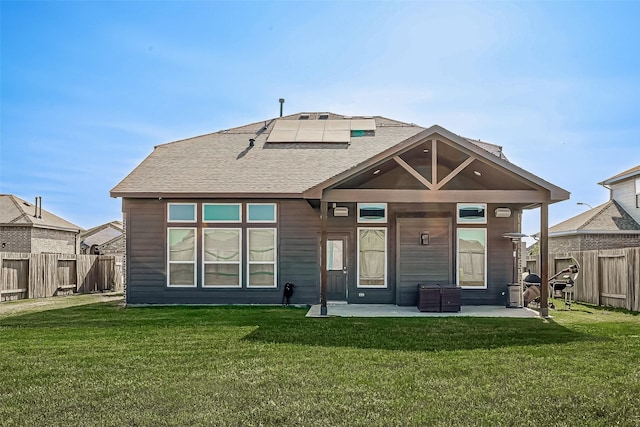 rear view of house with a patio area, a fenced backyard, roof mounted solar panels, and a yard