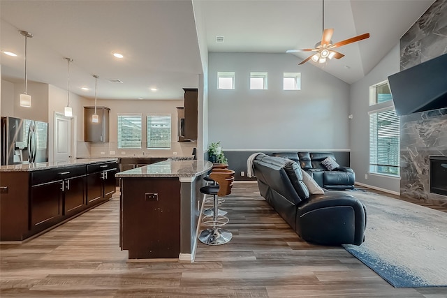 kitchen with stainless steel fridge with ice dispenser, a breakfast bar area, light stone counters, dark brown cabinets, and light wood-type flooring