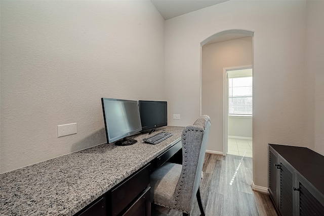 home office featuring arched walkways, dark wood-style flooring, and baseboards