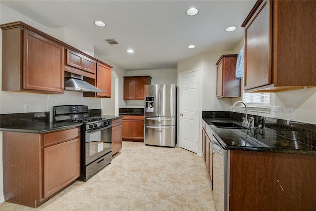 kitchen with visible vents, appliances with stainless steel finishes, a sink, wall chimney range hood, and dark stone counters