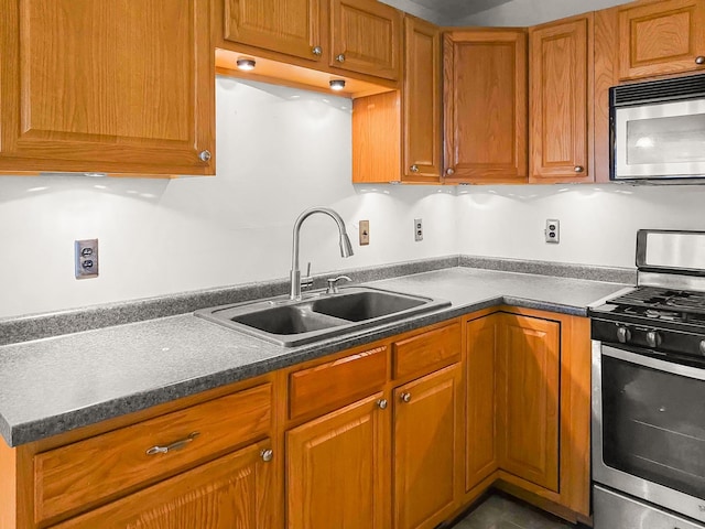 kitchen with stainless steel appliances, brown cabinetry, dark countertops, and a sink