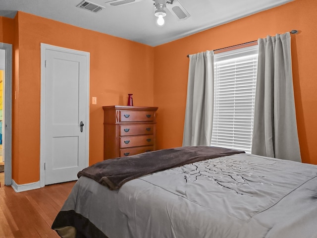 bedroom with ceiling fan, visible vents, and wood finished floors