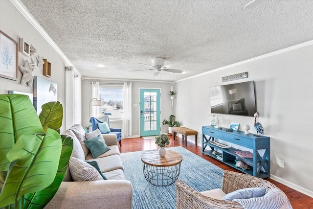 living room with ornamental molding, a ceiling fan, baseboards, and wood finished floors