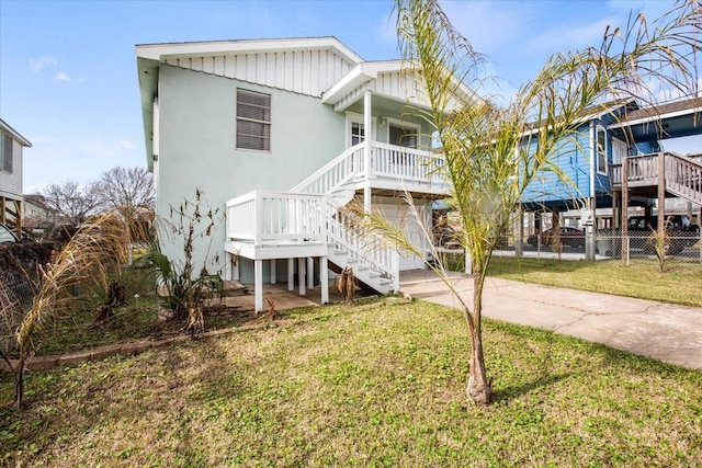 rear view of property featuring driveway, a lawn, stairway, fence, and a porch