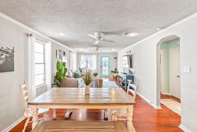 dining room featuring arched walkways, crown molding, visible vents, wood finished floors, and baseboards