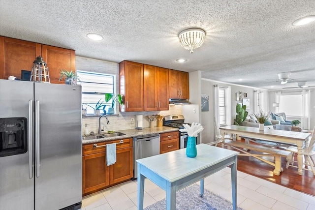 kitchen with brown cabinets, a sink, stainless steel appliances, under cabinet range hood, and a wealth of natural light