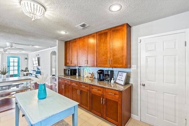 kitchen with brown cabinets, arched walkways, visible vents, and light stone countertops