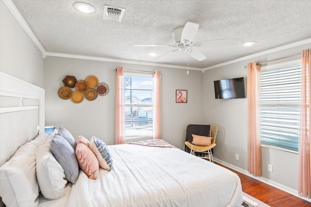 bedroom with a textured ceiling, wood finished floors, visible vents, baseboards, and ornamental molding