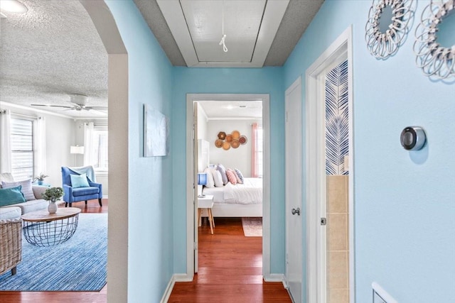 hall featuring arched walkways, a textured ceiling, baseboards, dark wood-style floors, and attic access