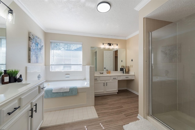 full bathroom with wood finished floors, a textured ceiling, crown molding, a shower stall, and two vanities