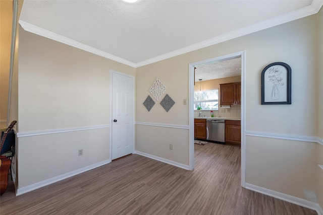 unfurnished room with ornamental molding, a textured ceiling, baseboards, and wood finished floors